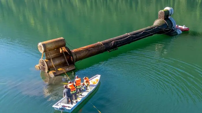 Eine technische Anlage schwimmt in einem See, daneben sieht man ein Boot mit mehreren Männern in Schutzkleidung