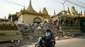 TOPSHOT - People ride a scooter past the rubble of damaged Buddhist pagoda in Mandalay on April 3, 2025, following the March 28 earthquake. The shallow 7.7-magnitude earthquake on March 28 flattened buildings across Myanmar, killing more than 3,000 people and making thousands more homeless. (Photo by Sai Aung MAIN / AFP)