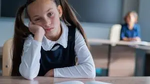 Little caucasian girl is bored at the lesson at school. The schoolgirl is sitting at her desk and the teacher is sitting in the background. Little caucasian girl is bored at the lesson at school. The schoolgirl is sitting at her desk and the teacher is sitting in the background Copyright: x RECORD DATE NOT STATED