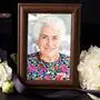 Ein Bilderrahmen mit einem Foto einer Frau mit weißen Haaren und buntem Kleid, nebenan liegen weiße Blumen | Gerlinde Mayer hinterlässt vier Kinder, zehn Enkelkinder und acht Urenkel