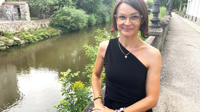Zu sehen ist eine Frau mit kinnlagen braunen Haaren. Im Hintergrund ist ein Fluss zu sehen