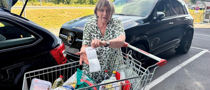Frau mit gefülltem Einkaufswagen zeigt Kassenbon