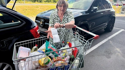 Frau mit gefülltem Einkaufswagen zeigt Kassenbon