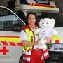 Eine Frau mit lockigen Haaren hat eine Rettungsuniform an und hält einen weißen Teddybären in der Hand