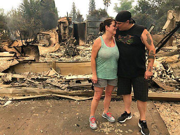 Ein Paar umarmt sich vor seinem Haus, das vom Carr-Feuer völlig zerstört worden ist