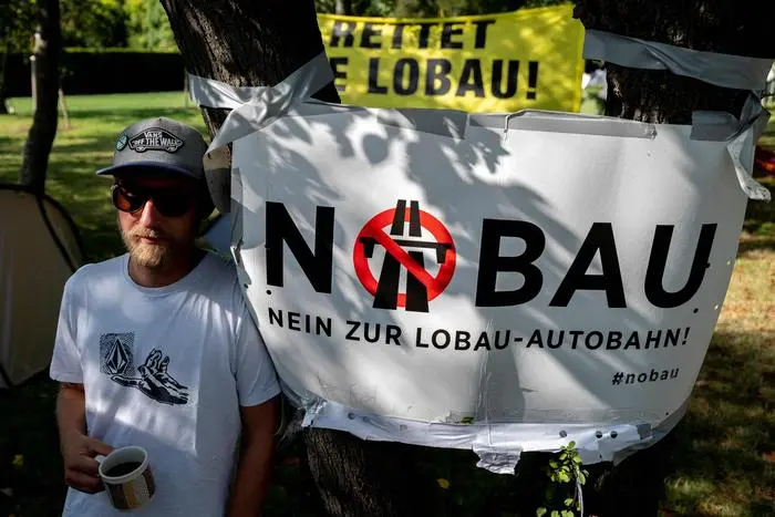 (FILES) This file photo taken on September 23, 2021 shows activist Florian Mayr standing next to a banner reading 'No Construction' at a camp set up by an alliance of activists of Fridays for Future, Jugendrat, Extinction Rebellion, System Change and others in a national park that they say is threatened by the construction of a highway in Vienna, Austria. - Austria's environment minister announced on December 1, 2021 the government was ordering a stop to several controversial highway construction projects, as part of the Green's pledge to fight climate change. Among those projects is the planned eight-kilometre (five-mile) highway tunnel under part of the Lobau national park to ease traffic flow east of Vienna. (Photo by JOE KLAMAR / AFP)