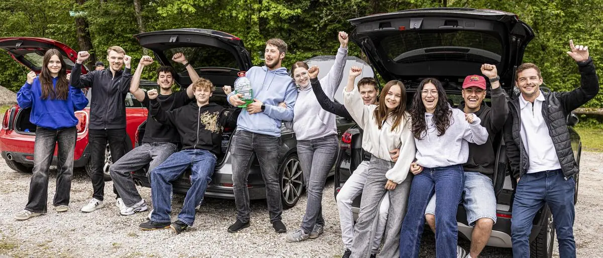 Man sieht viele junge Erwachsene vor ihren Autos jubeln