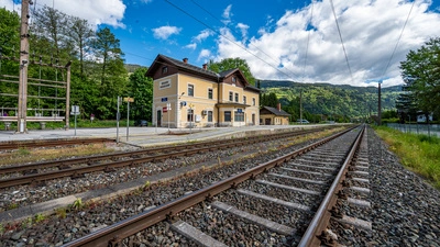 Zu sehen ist ein Bahngleis und dahinter ein kleiner Bahnhof.