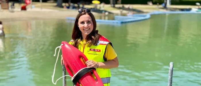 Eine Frau, Ende 20, in Einsatzkleidung vor einem See.