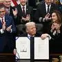 TOPSHOT - US President Donald Trump (C) shows the signed bill package to re-open the federal government as the Speaker of the House Mike Johnson (L) and other Republican leaders applaud in the Oval Office of the White House in Washington, DC, on November 12, 2025. Congress on Wednesday ended the longest government shutdown in US history, 43 days that paralyzed Washington and left hundreds of thousands of workers unpaid while Republicans and Democrats played a high-stakes blame game. The Republican-led House of Representatives voted largely along party lines to approve a Senate-passed package that will reopen federal departments and agencies, as many Democrats fume over what they see as a capitulation by party leaders. (Photo by Brendan SMIALOWSKI / AFP)