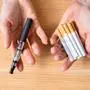 Woman's Hand Holding Vape And Tobacco Cigarettes Over Wooden Desk
