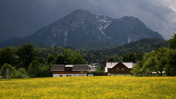 Häuser mit einem Berg im Hintergrund, wo sich Gewitterwolken bilden