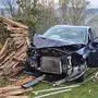 Das Bild zeigt ein schwer beschädigtes schwarzes Auto, das in den Holzstapel daneben gekracht ist | Die Feuerwehrleute bargen das Auto