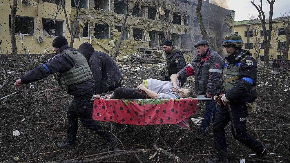 Das Bild zeigt eine offenbar schwangere Frau, die auf einer Liege durch Trümmer getragen wird