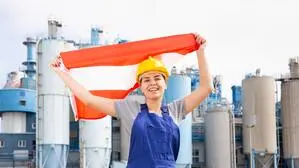 Frau in Arbeitskleidung mit Österreich-Fahne vor einem Industriegebäude