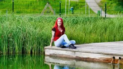Eine rothaarige Frau sitzt auf einem Steg und lächelt in die Kamera