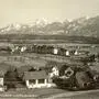 Eine schwarz-weiß Aufnahme mit Feldern und einigen Häusern. Im Hintergrund verschneite Berge | Der Villacher Stadtteil Völkendorf um 1930