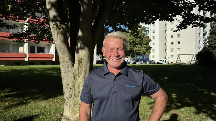 Ein älterer Mann steht vor einem Baum und lächelt in die Kamera