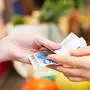 Hände übergeben zwei Euroscheine an der Kasse im Supermarkt
