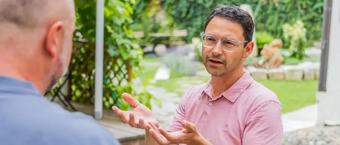Ein Mann mit Brille im Gespräch mit einem anderen Mann in einem Garten