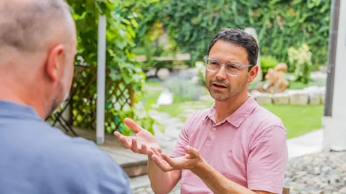 Ein Mann mit Brille im Gespräch mit einem anderen Mann in einem Garten 