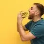 Young man eating tasty burger on color background. Space for text