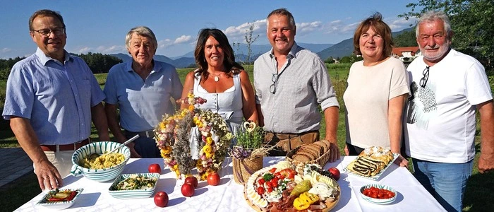 Zu sehen sind sechs Menschen, die sich um einen gedeckten Tisch versammeln. Darauf steht eine Erntekrone
