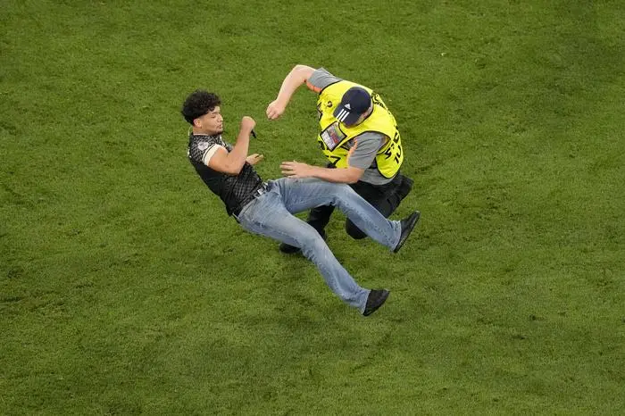 A spontaneous fan is knocked down by a steward after jumping onto the pitch at the end of a semifinal match between Spain and France at the Euro 2024 soccer tournament in Munich, Germany, Tuesday, July 9, 2024. (AP Photo/Ariel Schalit)