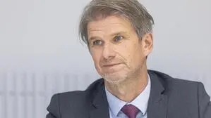 Mann mit grauen Haaren, Anzug und roter Krawatte blickt zur Seite