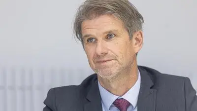 Mann mit grauen Haaren, Anzug und roter Krawatte blickt zur Seite