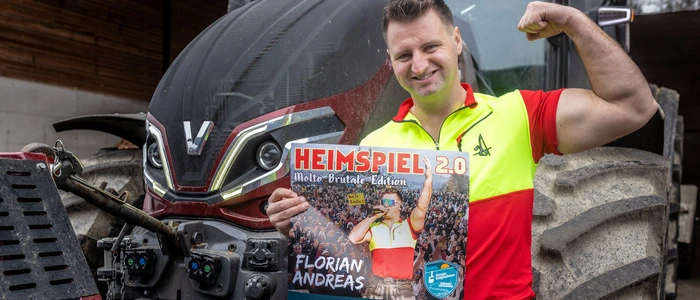 Der Sänger Florian Andreas steht mit einem Plakat vor einem Traktor