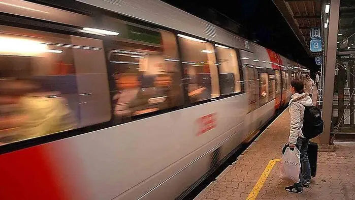 Ein Zug fährt in den Bahnhof, ein Schüler steht am Bahnsteig