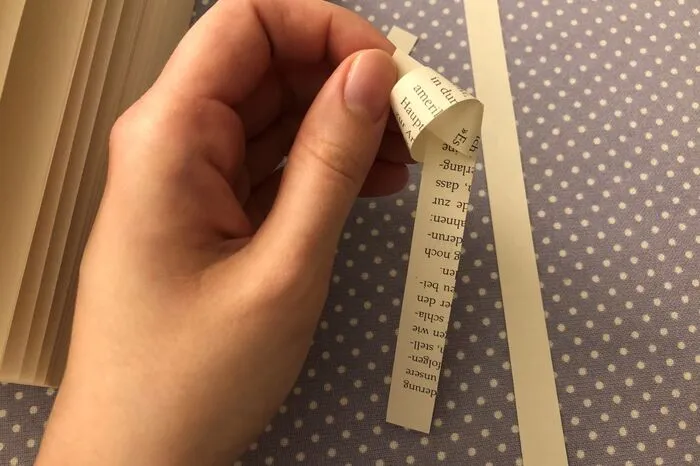 Wichtig ist, dass die Papierstreifen an jeder Stelle etwa gleich breit sind. In meinem Beispiel sind die Streifen, zur besseren Sichtbarkeit, etwa einen Finger breit. Sie können aber noch deutlich schmäler sein. Nun mache ich einen "Knoten" an das eine Ende eines Streifens...