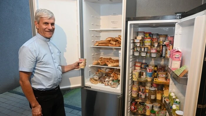 Ein Pfarrer steht neben einem Kühlschrank