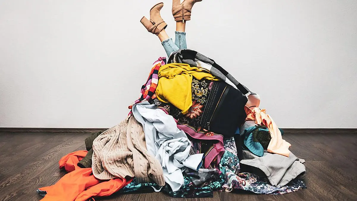 woman legs out of a pile of clothes on the floor. shopping addiction concept