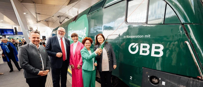 Drei Frauen und zwei Männer stehen auf einem Bahnhof vor einer grünen Lokomotive.