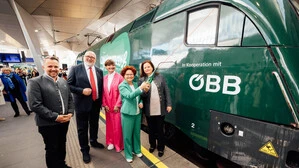Drei Frauen und zwei Männer stehen auf einem Bahnhof vor einer grünen Lokomotive.
