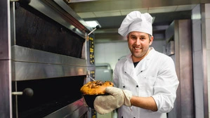 Ein Bäcker in seiner Backstube. Er hält einen Reindling in den Händen.