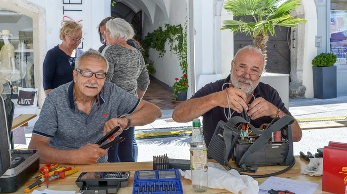 Zwei ältere Herren sitzen mit Werkzeug an einem Tisch 