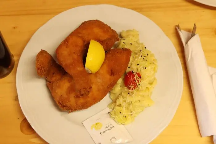 Denn im Mittelpunkt steht das Backhendl. Goldbraun gebacken und mit Kartoffelsalat serviert, kommt es frisch auf den Teller. Dazu ein kühles Bier – für viele Wiesenmarkt-Besucher ist diese Kombination ein fixer Bestandteil ihres Wiesn-Besuchs. Neben dem Backhendl (18,90 Euro) ist auch das Wiener Schnitzel (17,50 Euro) ein Renner. 