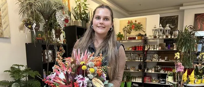 Eine junge Frau steht mit Blumen vor einem Geschäft