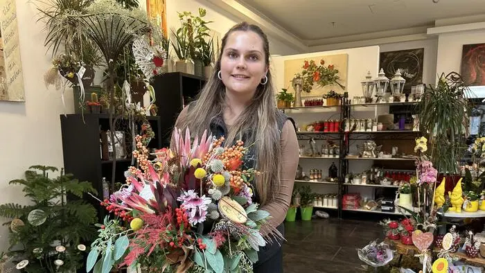 Eine junge Frau steht mit Blumen vor einem Geschäft