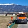 Oranges Fahrzeug der Straßenmeisterei, zwei Männer stellen grünen Amphibienschutzzaun auf, schneebedeckter Berg im Hintergrund