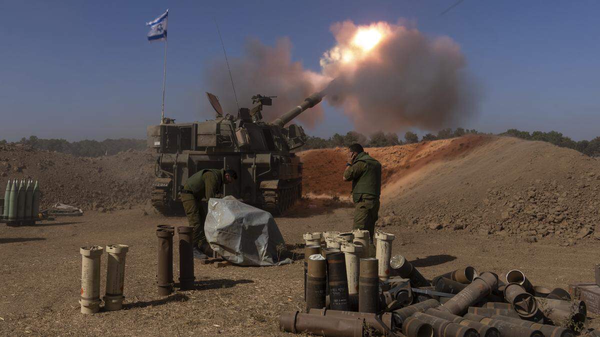 Ein mobiles Artilleriegeschütz der IDF im Moment des Abschusses eines Geschosses auf ein Ziel im Gazastreifen. Gerät steht auf staubiger Erde, umgeben von einem kleinen aufgehäuften Erdwall. Dahinter Soldaten. | Israelische Artillerie beschießt ein Ziel im Gazastreifen
