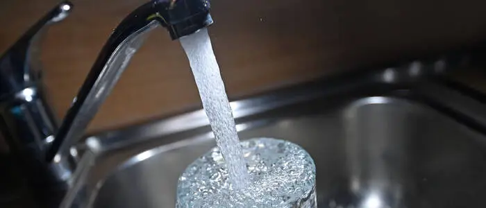 Ein laufender Wasserhahn, es wird ein Glas aufgefüllt.