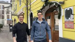 Zwei junge Männer stehen vor dem Eingang eines Gasthauses