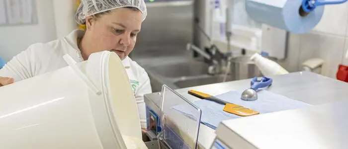 Eis-Produzentin Petra Pobaschnig schüttet Milch in ein Produktionsgerät. Sie ist in weiß gekleidet und trägt ein Haarnetz