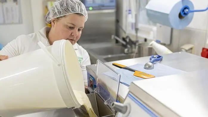Eis-Produzentin Petra Pobaschnig schüttet Milch in ein Produktionsgerät. Sie ist in weiß gekleidet und trägt ein Haarnetz