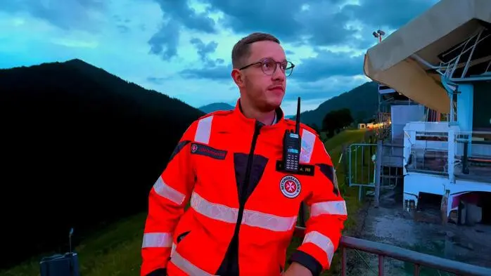 Ein Mann, Anfang 20, steht in einer orangen Uniform in der Abenddämmerung in der Natur