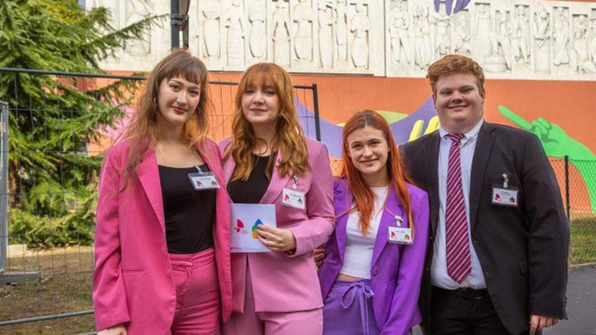 Das Projektteam Laura Moderer, Lisa-Marie Kriegler, Clara Lozinsek und Nathanael Schatz vor dem Relief – links das alte Relief mit den traditionellen Figuren, rechts die moderne Erweiterung